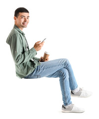 Canvas Print - Young guy with mobile phone and cup of coffee sitting in chair on white background