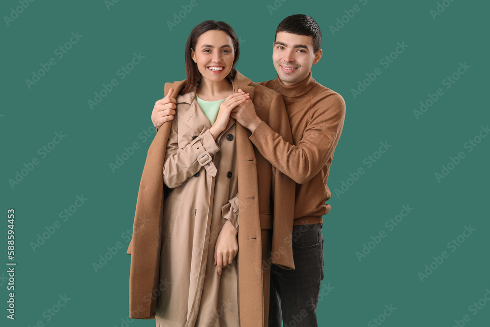 Young man putting coat onto his girlfriend on green background