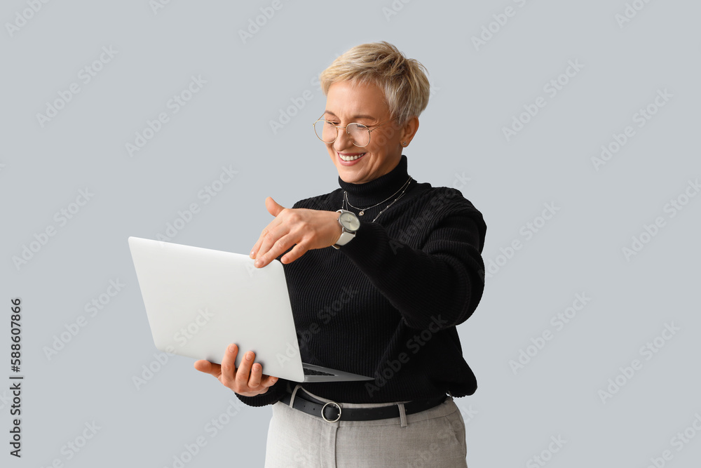 Beautiful mature woman with laptop on light background