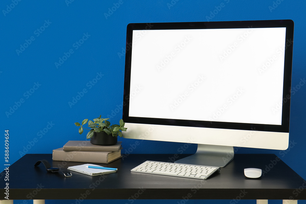 Workplace with computer, smartwatch and books near blue wall