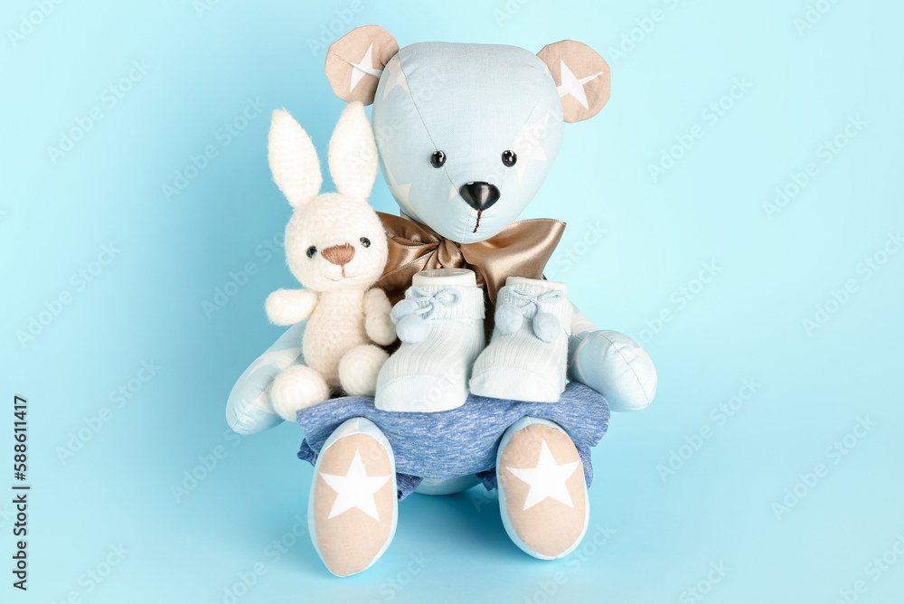 Toy bear and bunny with baby clothes on blue background