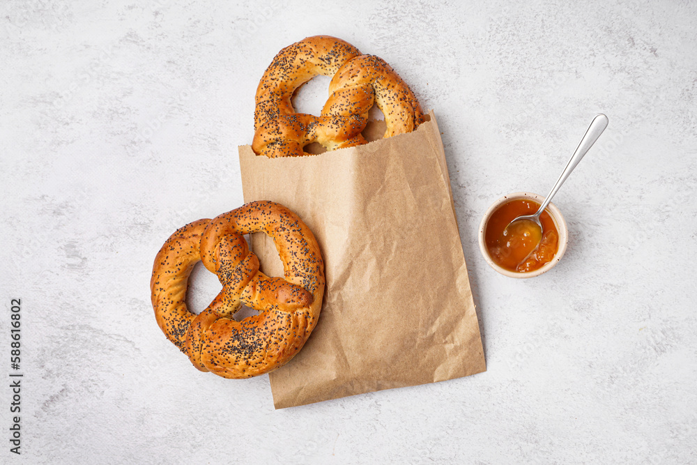 Paper bag with tasty pretzels and jam on light background