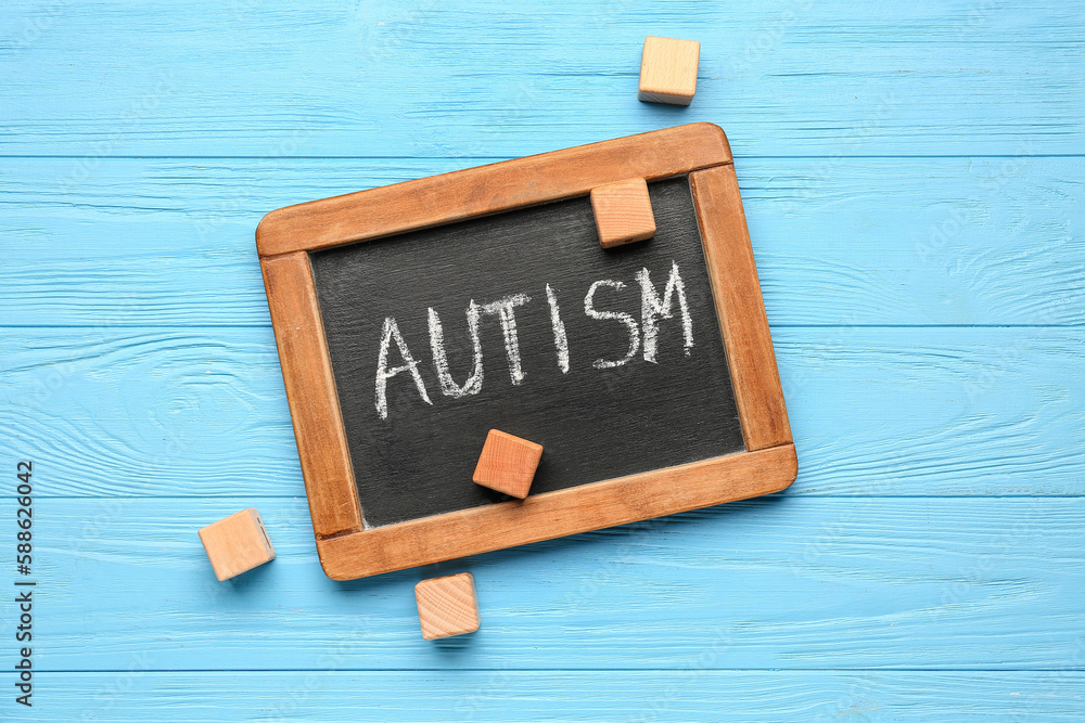 Chalkboard with word AUTISM and cubes on blue wooden background