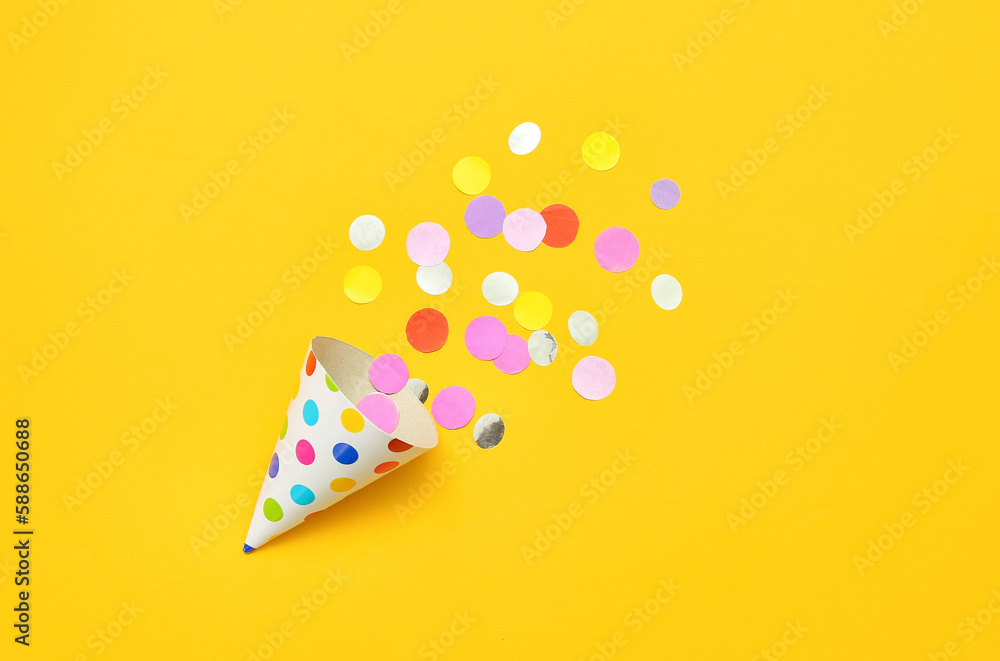 Composition with party hat and confetti on yellow background