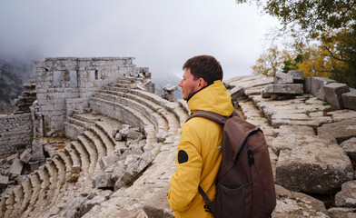 Wall Mural - Autumn walk , man in yellow jacket looks at the ancient amphitheatre in city Termessos Ancient City, Turkey. Turkeys most outstanding archaeological sites and one of main tourist center.
