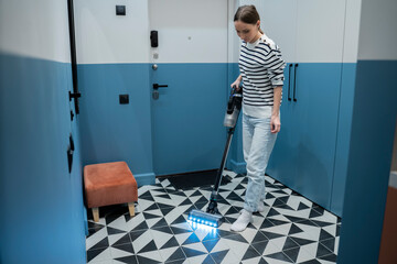 Sticker - Young woman vacuums the floor in the hallway next to the front door. 