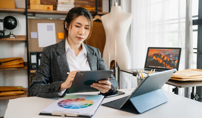 Fashion designer l young asian woman working using laptop, tablet and smiling while standing in workshop Responding