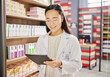 © Nina/peopleimages.com - Pharmacist, tablet and Asian woman in pharmacy for healthcare or online consultation in drugstore. Telehealth, technology and happy person or medical professional with touchscreen for shop research.