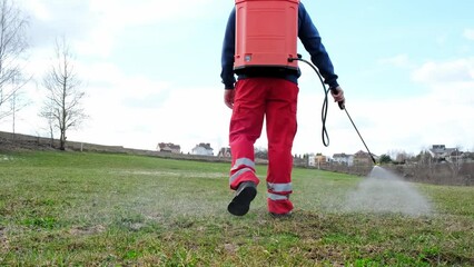 Wall Mural - Farmer spraying pesticide on lawn field wearing protective clothing. Treatment of grass from weeds and dandelion. Pest control. Insecticide sprayer with a proper protection. Gardening care season.