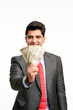 © Niks Ads - Young indian man in suit and showing indian rupees on white background.