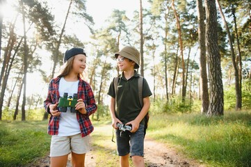 Wall Mural - Happy excited school children with backpacks in casual clothes enjoying walk in forest on sunny autumn day, two active kids boy and girl running and playing together during camping trip in nature.