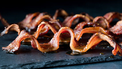 Wall Mural - wavy strips of crispy maple pepper bacon on a black slate board.