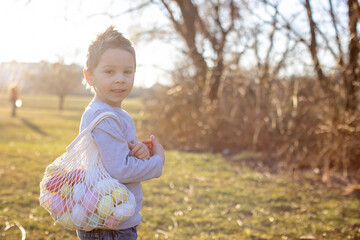 Wall Mural - Cute toddler boy, gathering easter colorful eggs in a basket in the park