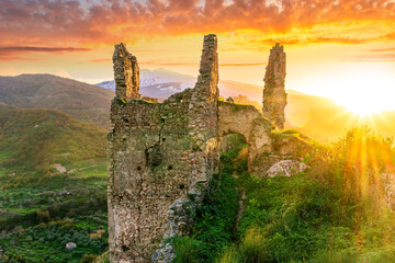 immersive landscape of old castle ruins on foreground and beautiful mountains with sunset with clouds on background