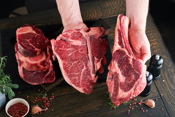 Wall Mural - Chef cutting steak beef. Mans hands hold raw steak Tomahawk on rustic wooden cutting board on black background. Cooking, recipes and eating concept. Selective focus.