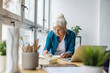 © pikselstock - Smiling mature businesswoman writing in notebook while sitting at table in office