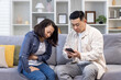 © Liubomir - Family couple man and woman sitting on sofa at home asian family man trying to call doctor for sick wife.