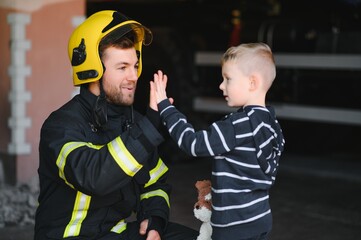 Wall Mural - Portrait of rescued little boy with firefighter man standing near fire truck. Firefighter in fire fighting operation.