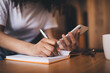 © BullRun - Faceless woman writing in notepad while sitting with smartphone at table