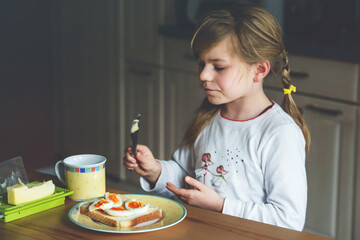 Wall Mural - Little smiling girl have a breakfast at home. Preschool child eating sandwich with boiled eggs. Happy children, healthy food and meal.