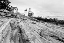Pemaquid Point Lighthouse, Maine. View Of Lighthouse And Keeper's House From The Bottom Of Rocky Cliff Looking Upwards Towards Lighthouse Sitting On Top Of The Promontory. Black And White.