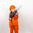 © Plutmaverick - Little girl in an orange suit and construction helmet, holding puncher, concept of young worker. Portrait, child builder, white background, Labor Day.