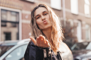 Wall Mural - Pensive blonde woman turn back and make blow kisses on the street. Outdoor shot of happy hippie lady with two thin braids and wave hair. Boho freedom style. Girl send air kiss to camera, love concept.