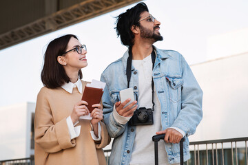 Smiling young international man and female in casual and glasses look up at sky, at free space in airport