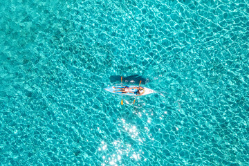 Aerial view of kayak with people in blue sea at summer sunny day. Man and woman on floating canoe in clear azure water. Sardinia island, Italy. Tropical landscape. Sup board. Active travel. Top view