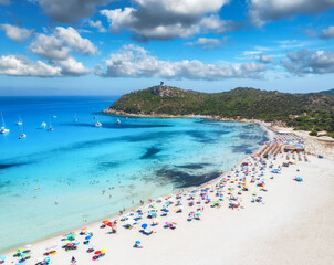 Aerial view of colorful umbrellas, white sandy beach, people, boats and yachts in blue sea, mountain, sky with clouds at summer sunny day. Tropical landscape. Travel in Sardinia, Italy. Top drone view