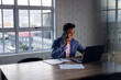 © Wavebreak Media - Happy biracial businessman at desk, using laptop and talking on smartphone, working late at office