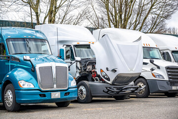 White big rig semi truck with open hood performs routine inspection and repairs right in the parking lot next to other parked semi trucks