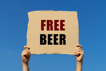 Free beer text on box paper held by 2 hands with isolated blue sky background. This message board can be used as business concept about dinking beer for free.