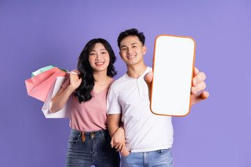 Wall Mural - image of asian couple holding shopping bags on purple background