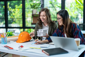 Concept of engineering consulting, Two female engineers discussing about model of building together; Two female architects are studying blueprint of building house.