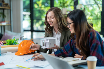 Concept of engineering consulting, Two female engineers discussing about model of building together; Two female architects are studying blueprint of building house.