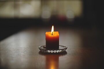 Sticker - Closeup shot of a lit candle on a glass saucer with a reflection on a wooden table