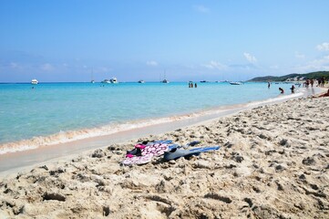 Rubber fins on the sandy beach with people against the background of the sea with boats.