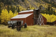 Red Wooden Barn And Old Tractor Surrounded By Yellow Aspen Trees In The Countryside In Colorado