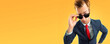 Are you seriously?! Funny skeptic businessman in grey confident suit and red tie, looking through eye sunglasses, copy space text area, isolated on yellow-orange background. Wide banner image.