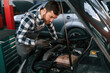 © standret - Repairing the electronics of the car under the hood. Man in uniform is working in the auto salon