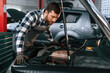 © standret - Repairing the electronics of the car under the hood. Man in uniform is working in the auto salon