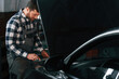 © standret - Black car is repairing. Hood is opened. Man in uniform is working in the auto salon