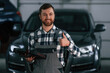 © standret - Showing gesture and smiling. Holding tablet. Man in uniform is working in the auto salon