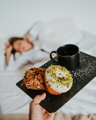 Sticker - Closeup of a man serving delicious donuts and a cup of coffee to a girl sleeping in bed