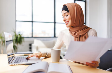 beautiful smiling muslim woman in traditional religious hijab works remotely on laptop from home