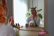 Young woman with multicolored hair sitting by the mirror and applying lip balm with a maltese dog sitting on her lap. Morning beauty routine concept. Close up, copy space, background.