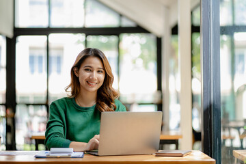 young woman working in a cafe using laptop and drinking coffee Asian female student using a computer for distance learning sitting on a bench in the shop casual lifestyle people and technology lifesty