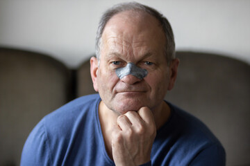 smiling senior man applying black nose patch to clean pore skin and remove acne or blackheads on nos
