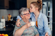 © Iryna - Loving teen granddaughter and grandmother embracing, drinking tea in kozy kitchen at home. Special moments together. an attractive woman visiting granny for tea.